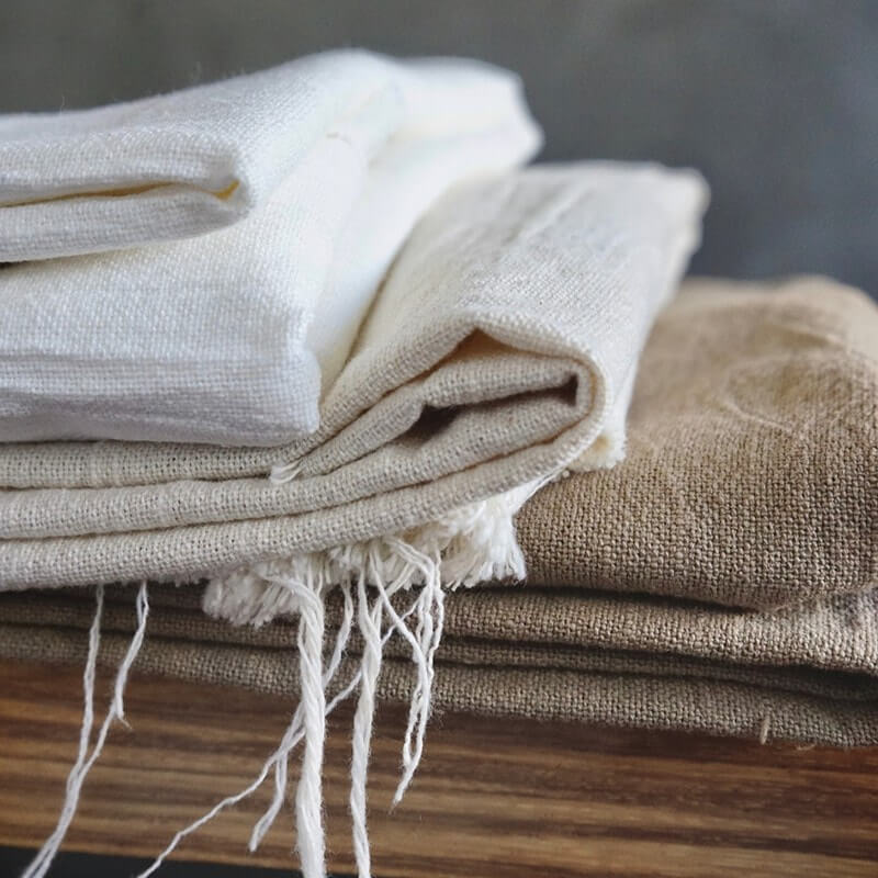 Four-beige-folded-linen-pieces-are-placed-on-the-wooden-table.